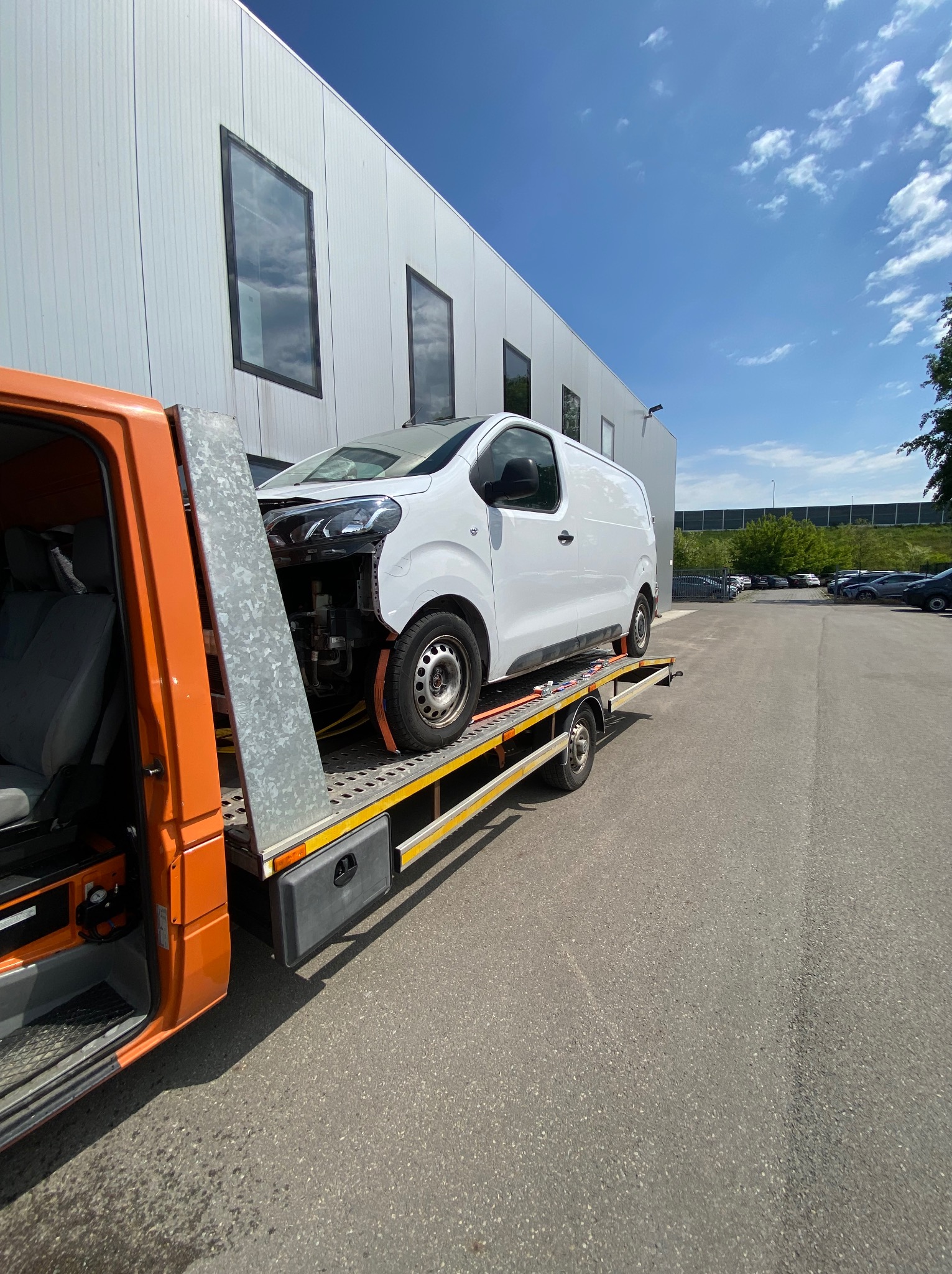 Laweta z uszkodzonym busem w Bytomiu. Pomarańczowy pojazd z białym busem na platformie, widoczny fragment budynku w tle.
