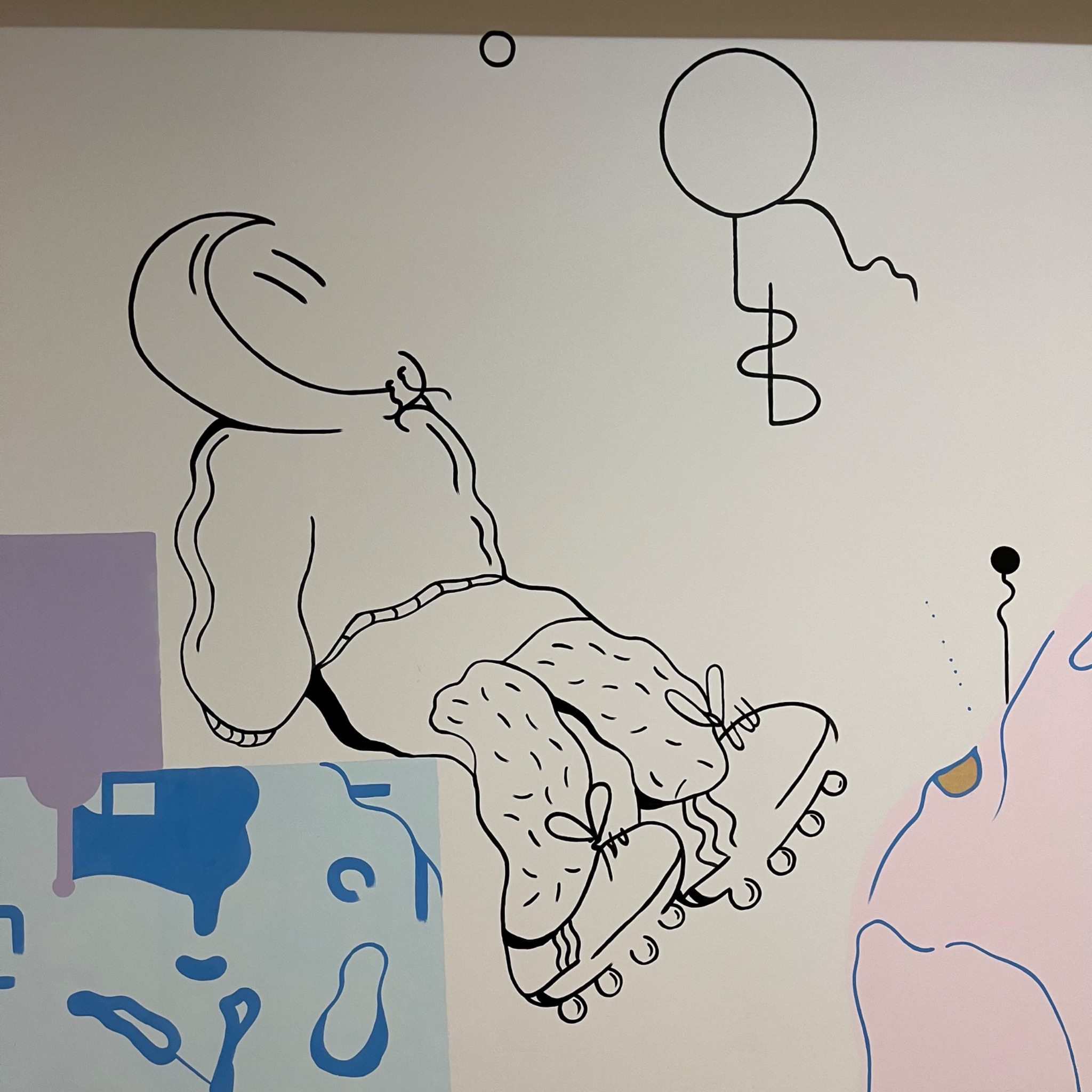 Abstrakcyjna kompozycja na ścianie przedstawiająca postać w bluzie i rolkach, z dodatkowymi elementami graficznymi w stylu minimalistycznym.