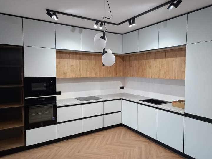 Nowoczesna kuchnia z białymi i drewnopodobnymi frontami, oświetleniem szynowym i podłogą ułożoną w jodełkę.