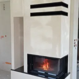 Nowoczesny kominek narożny z czarnymi akcentami i płomieniami, widoczny w surowym wnętrzu, prawdopodobnie w trakcie wykańczania.