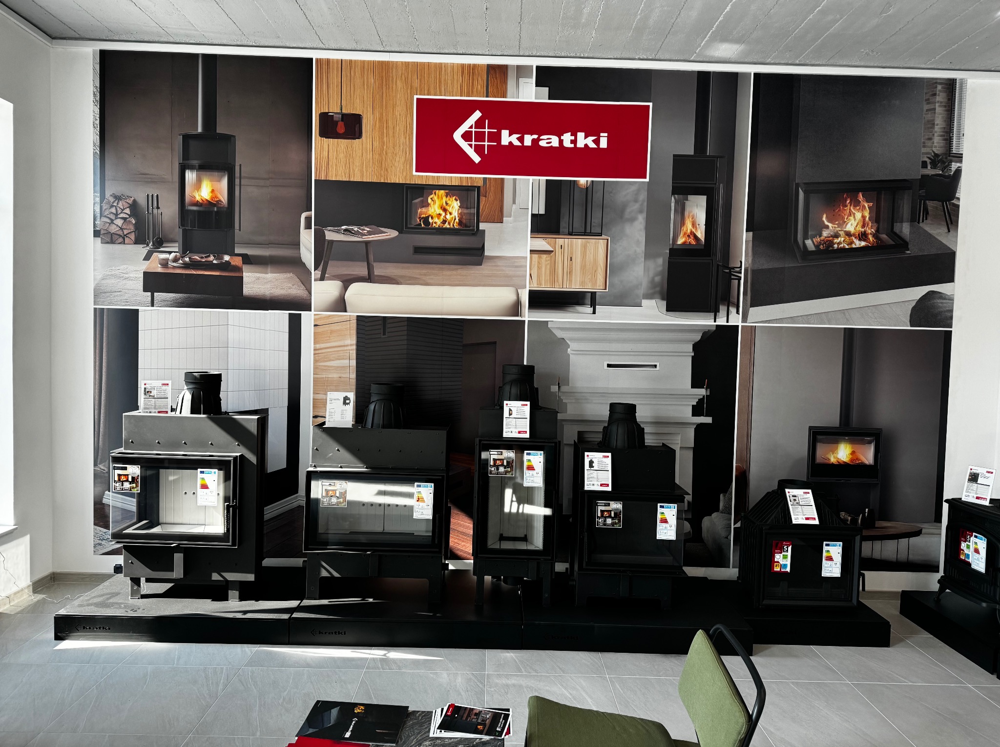 Ekspozycja modeli wkładów kominkowych marki Kratki w salonie, na tle dużego plakatu z aranżacjami wnętrz z kominkami.