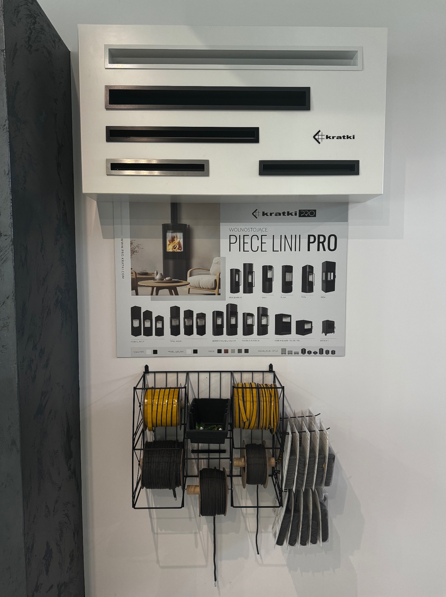 Ekspozycja kominków Kratki: modele w obudowach, kratki wentylacyjne, akcesoria montażowe na ścianie w sklepie.