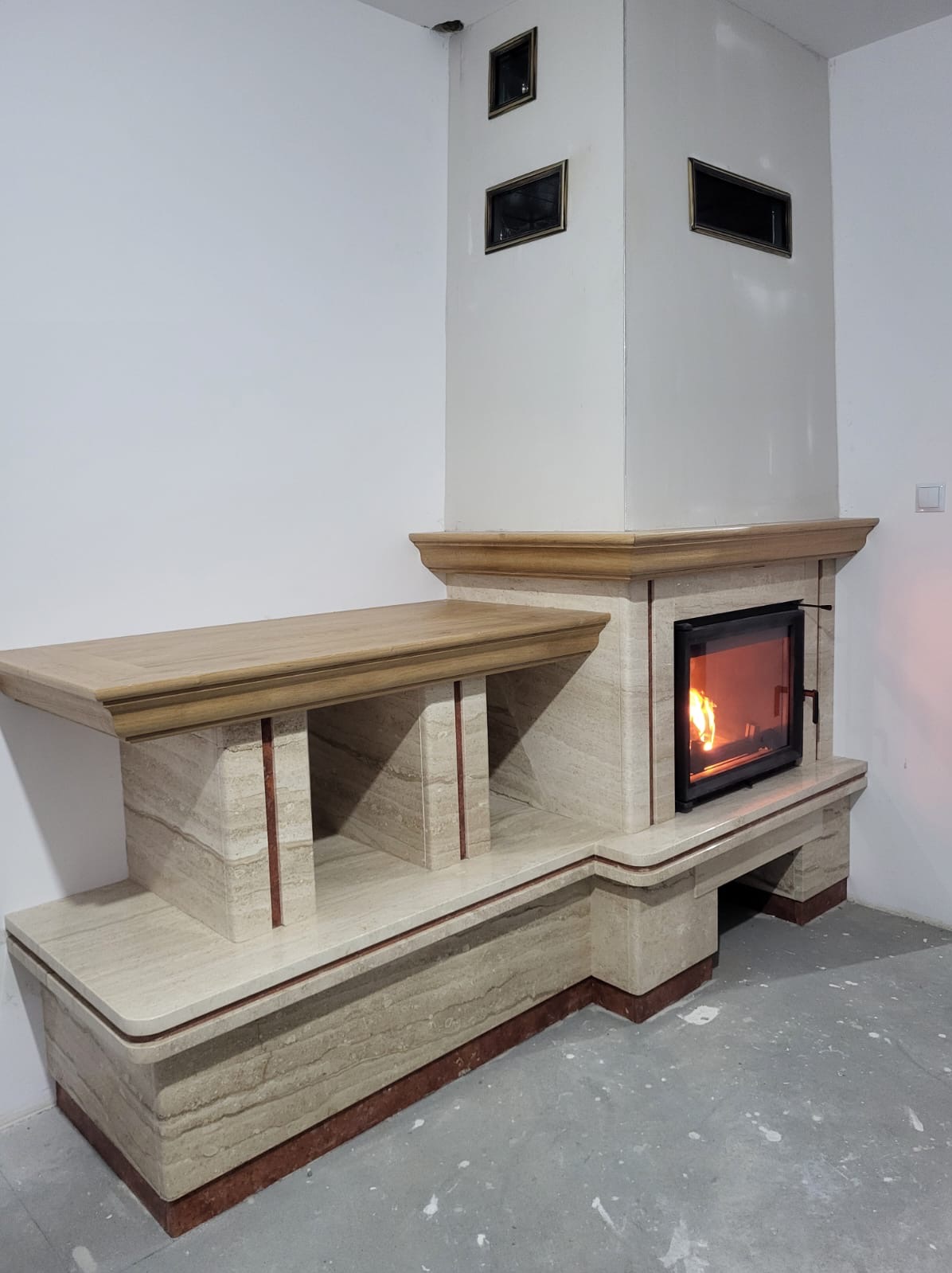 Wykończony kominek z obudową z trawertynu i drewnianym blatem w Kolbuszowej Dolnej. Wkład kominkowy z paleniskiem, kratki wentylacyjne.