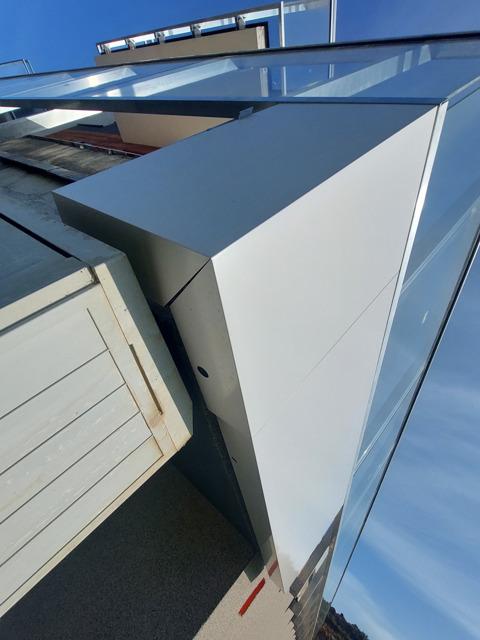 Nowoczesna szklana balustrada z elementami metalowymi, uchwycona pod nietypowym kątem, ukazująca refleksy nieba i sąsiadującego budynku.