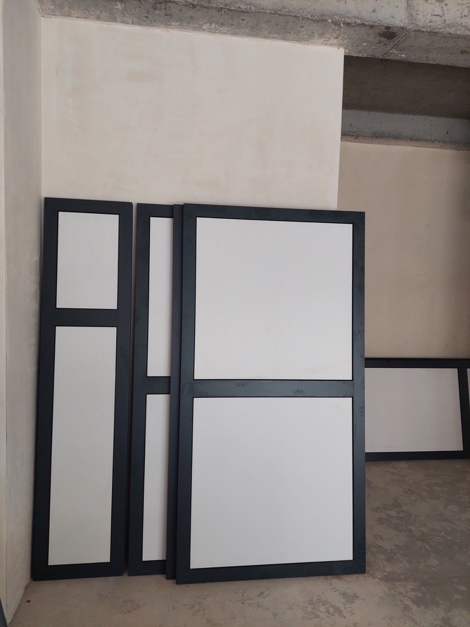 Przygotowane do montażu panele szklane z czarnymi ramami, oparte o ścianę w surowym wnętrzu.