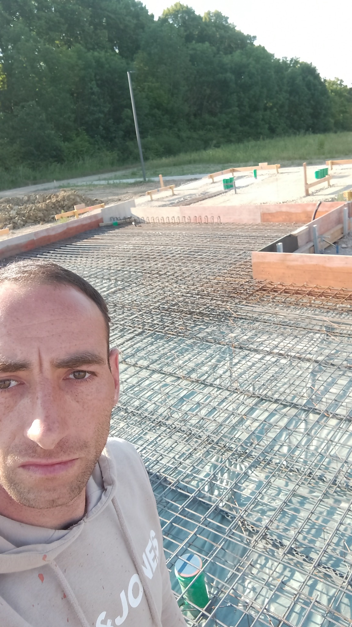 Zbrojenie fundamentu z widocznymi szalunkami drewnianymi i zielonymi rurkami, ujęcie z perspektywy osoby pracującej na budowie.