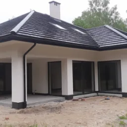 Nowoczesny dom jednorodzinny z białą elewacją, czarnym dachem z dachówki ceramicznej i dużymi oknami, widok z zewnątrz na surowy stan wykończenia terenu.