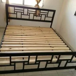 Rama łóżka metalowego z drewnianym stelażem, czarna konstrukcja z geometrycznym wzorem, widok z przodu w jasnym wnętrzu.