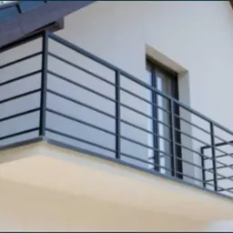 Nowoczesna, czarna, metalowa balustrada balkonowa z poziomymi szczeblami na tle białej elewacji domu z brązowym dachem.