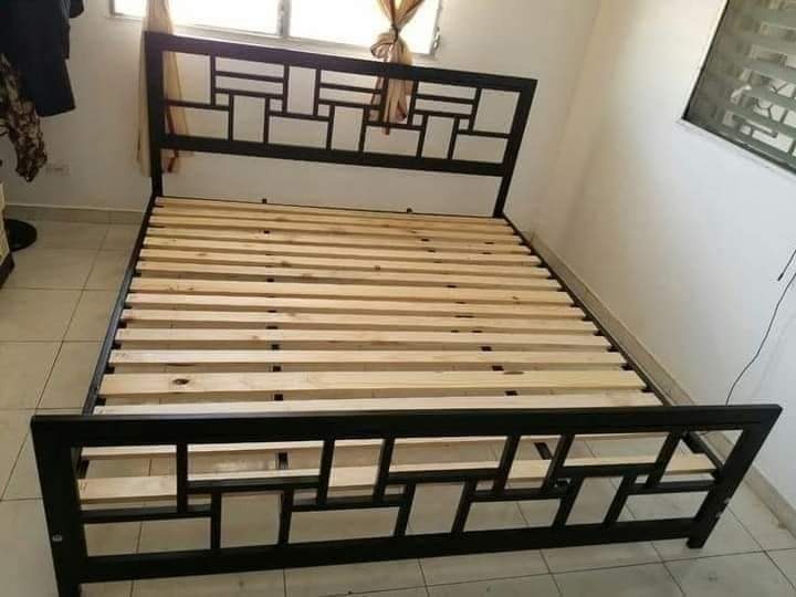 Rama łóżka metalowego z drewnianym stelażem, czarna konstrukcja z geometrycznym wzorem, widok z przodu w jasnym wnętrzu.