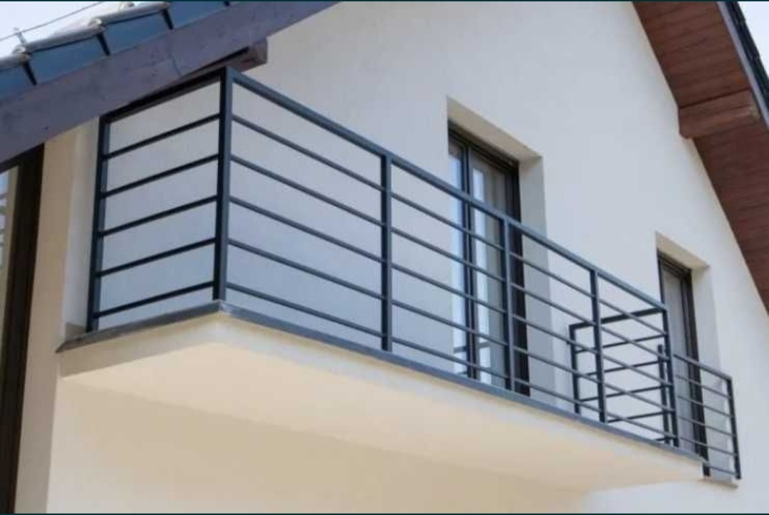 Nowoczesna, czarna, metalowa balustrada balkonowa z poziomymi szczeblami na tle białej elewacji domu z brązowym dachem.