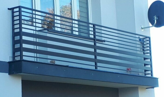 Nowoczesna balustrada balkonowa z poziomych, metalowych profili w kolorze grafitowym, zamontowana na jasnej elewacji budynku, widoczna antena satelitarna.