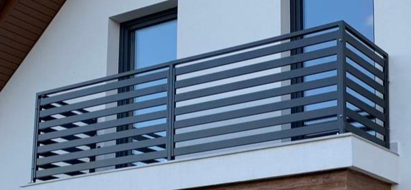 Nowoczesna, szara, pozioma balustrada balkonowa z metalowych profili, zamontowana na białym budynku z widocznym oknem.