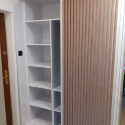 Davi Meble - Biała szafa wnękowa z przesuwnymi drzwiami z drewnianymi lamelami, widoczna część z półkami, zamontowana w mieszkaniu w Nowym Sączu.