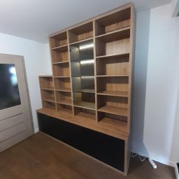 Davi Meble - Drewniana szafa wnękowa z oświetleniem LED w Nowym Sączu, z czarną podstawą, widoczna na tle białej ściany i drewnianej podłogi, obok drzwi.