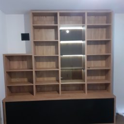 Davi Meble - Drewniany regał na wymiar z czarną podstawą, oświetlenie LED w jednej sekcji, widoczne półki i prosta forma.