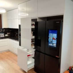 Davi Meble - Biała kuchnia na wymiar z szafkami cargo, czarnym blatem i nowoczesną lodówką z ekranem dotykowym.