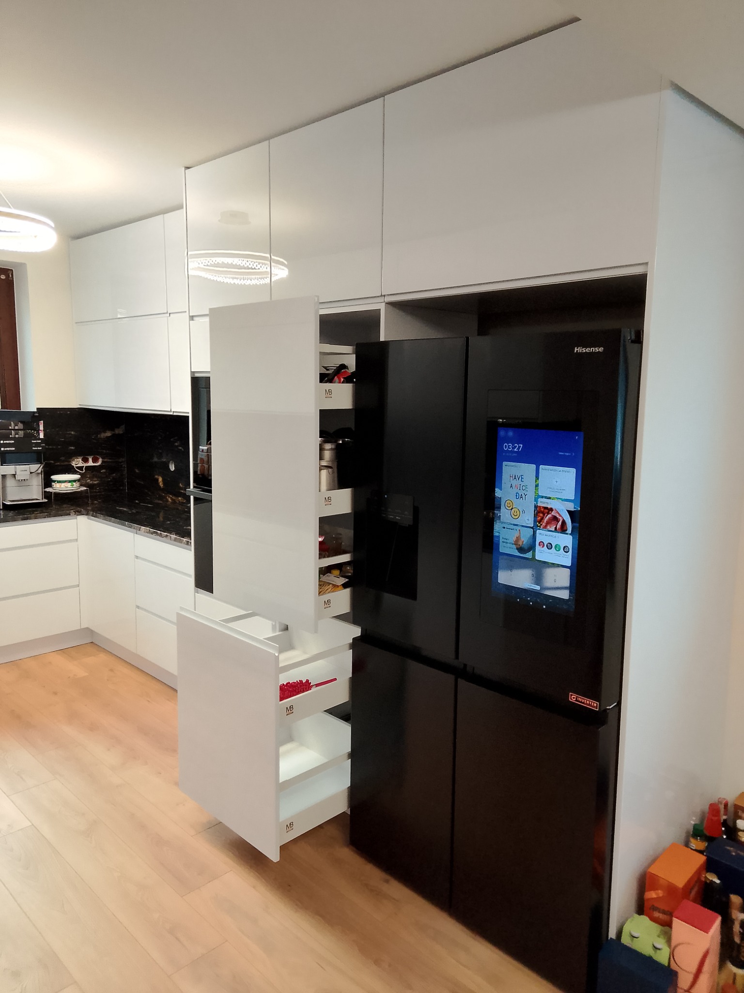 Biała kuchnia na wymiar z szafkami cargo, czarnym blatem i nowoczesną lodówką z ekranem dotykowym.