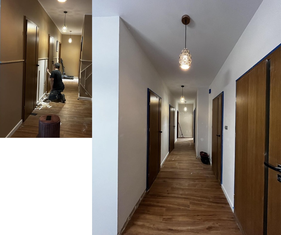 Korytarz w trakcie malowania: ściany pomalowane na biało, drewniane drzwi z niebieską taśmą malarską, podłoga w panelach imitujących drewno, ozdobne lampy sufitowe, widoczny pracownik w trakcie...