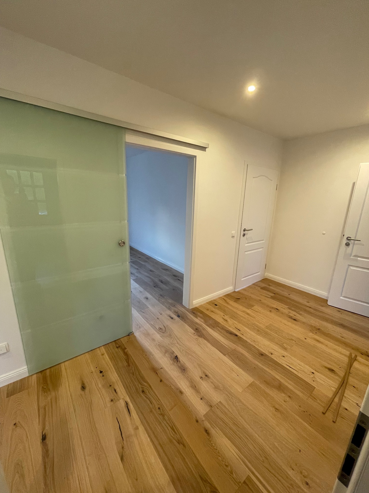 Wnętrze pokoju po remoncie z drewnianą podłogą, przesuwnymi drzwiami ze szkła mlecznego i dwiema białymi drzwiami po prawej stronie.