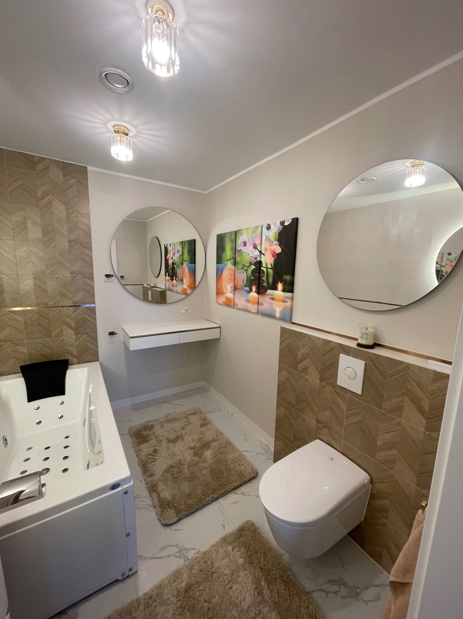 Nowoczesna łazienka z wanną jacuzzi, wiszącą toaletą, okrągłymi lustrami i panelami ściennymi w odcieniach beżu i brązu.