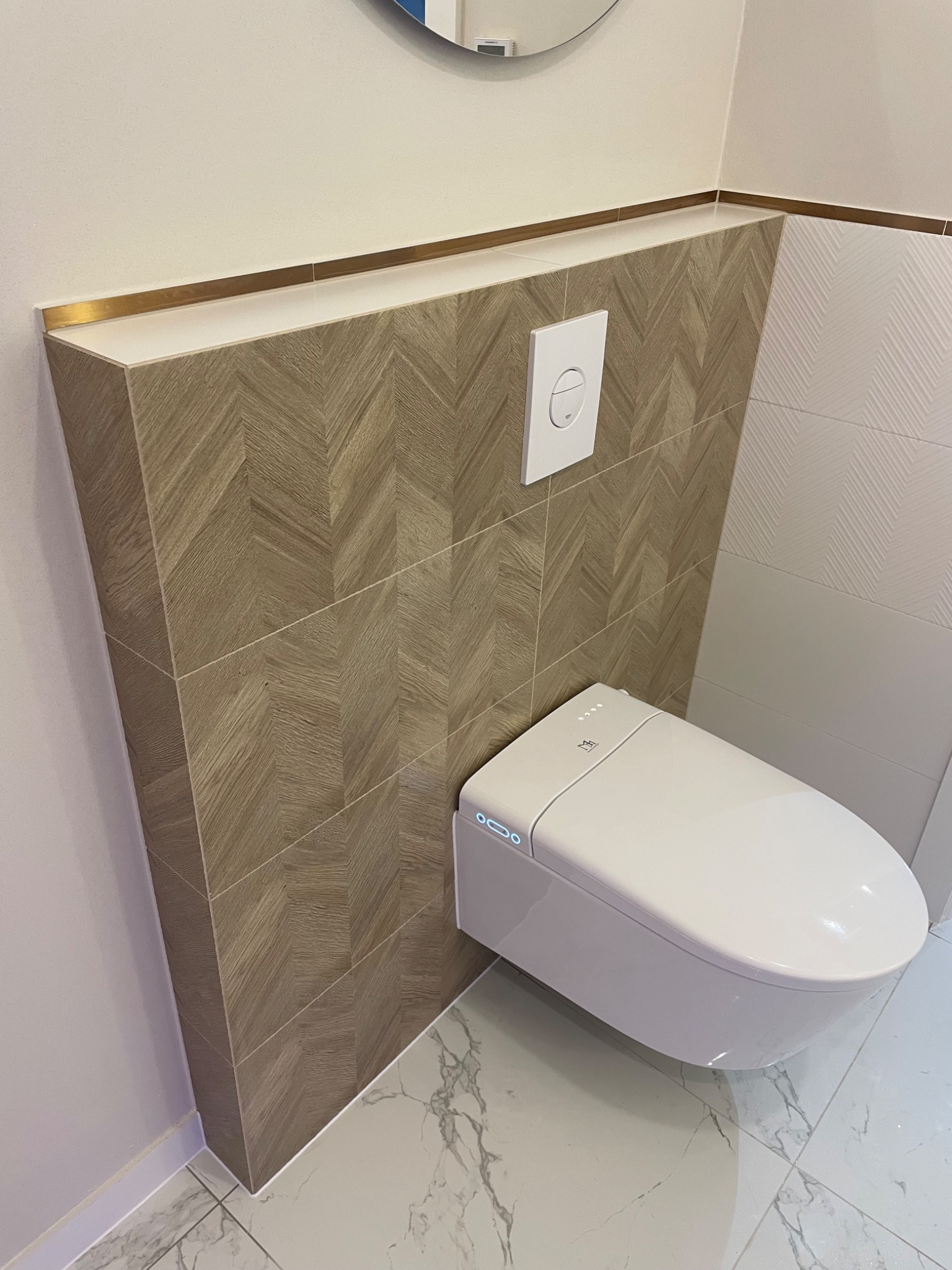 Nowoczesna toaleta podwieszana z deską elektroniczną i przyciskiem spłukującym na ścianie wykończonej płytkami w jodełkę, marmurowa podłoga.