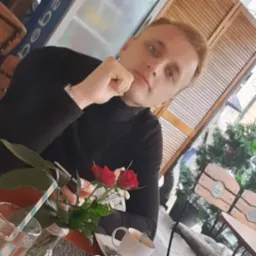 Portret młodego mężczyzny w czarnym golfie, siedzącego przy stoliku kawiarnianym z drinkiem, bukietem czerwonych róż i filiżanką kawy, prawdopodobnie podczas przerwy w pracy nad projektem.