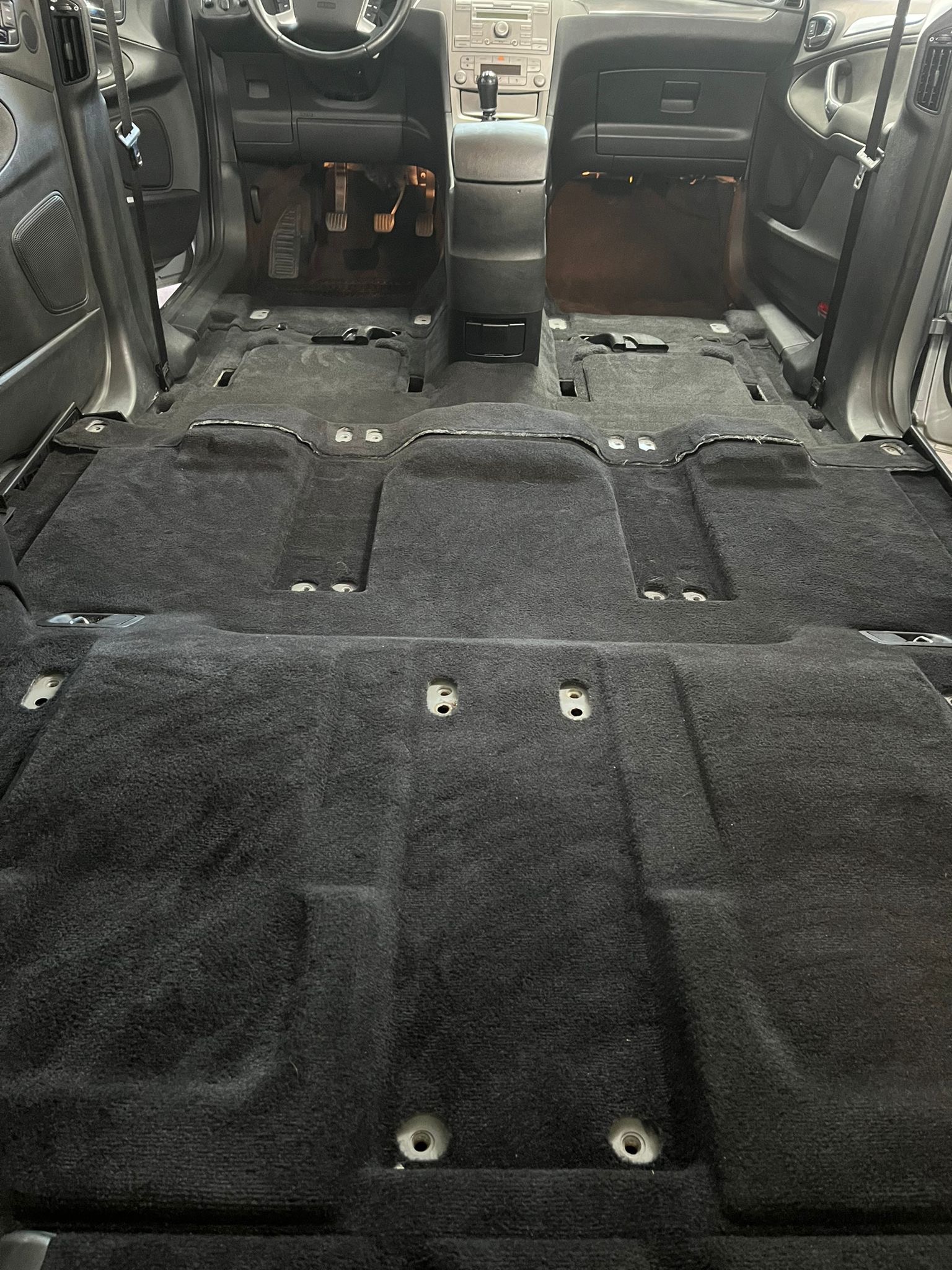 Wnętrze samochodu z wyjętymi siedzeniami i odsłoniętą czarną wykładziną podłogową, przygotowane do czyszczenia lub naprawy.