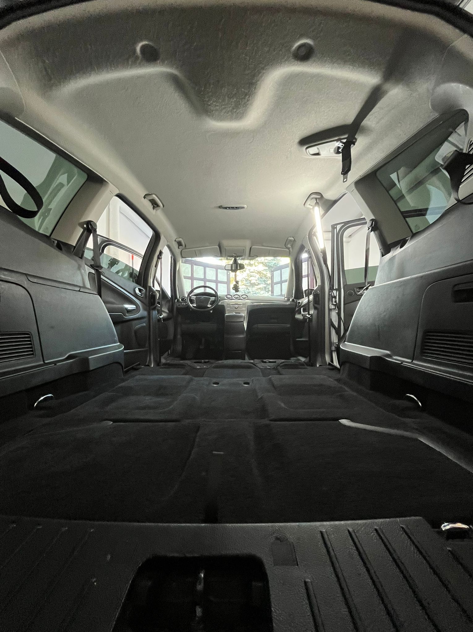 Wnętrze bagażnika i przedziału pasażerskiego samochodu typu van, z widocznymi elementami mocującymi ładunek i otwartymi drzwiami bocznymi.