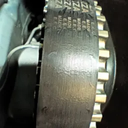 Zużyty pasek rozrządu E.E.C. E7ZA na kole zębatym w silniku samochodowym, widoczne ślady eksploatacji i otarcia.