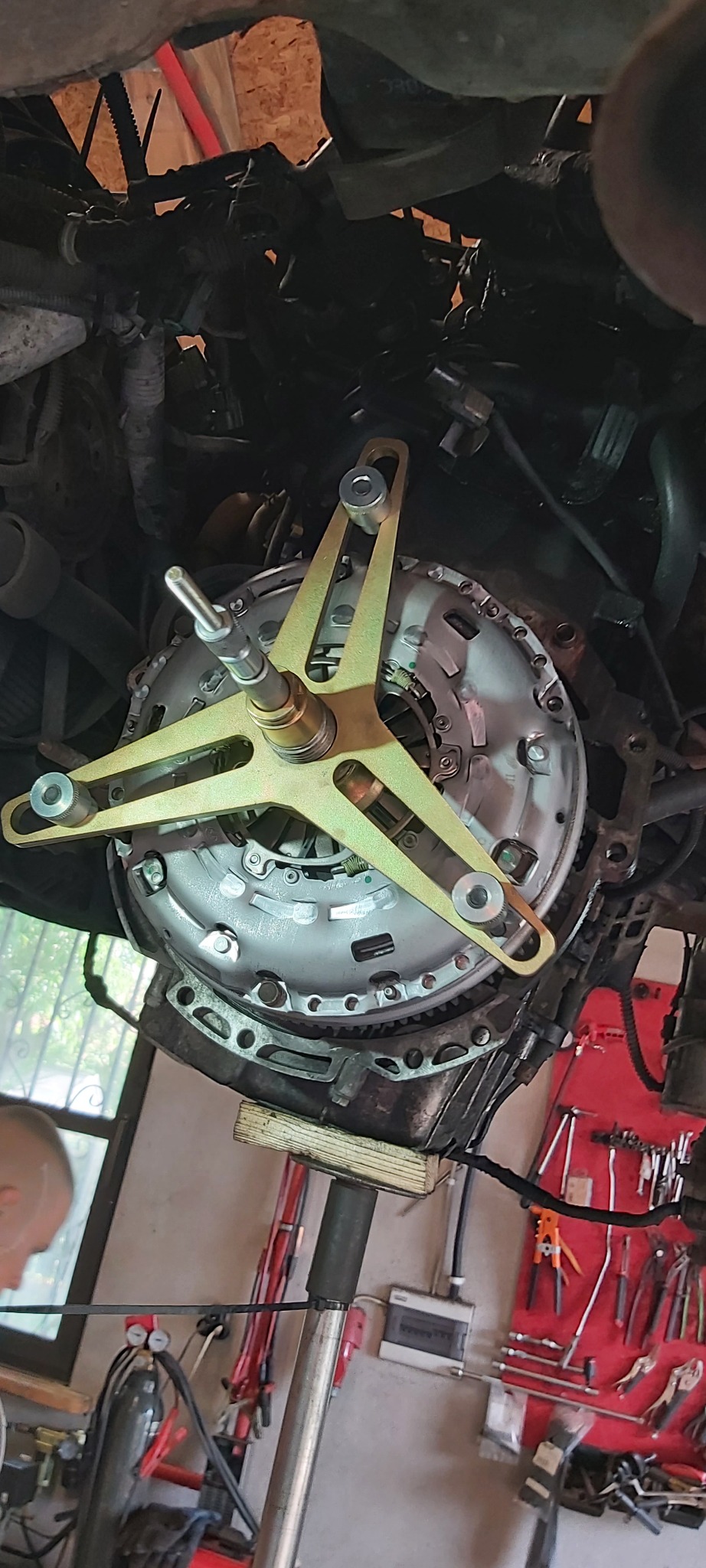 Sprzęgło samochodowe zamontowane na specjalnym narzędziu do centrowania przed przykręceniem, widoczne z dołu pojazdu w warsztacie.