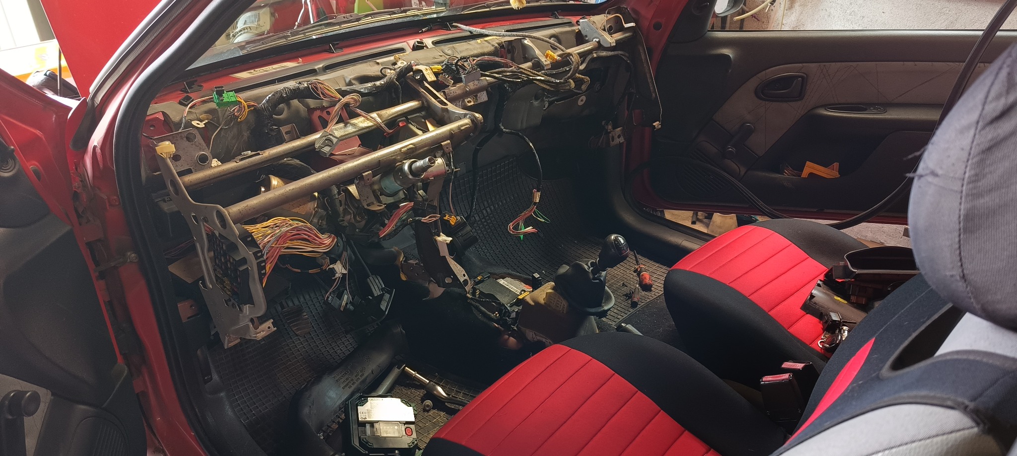Wnętrze czerwonego samochodu w trakcie demontażu deski rozdzielczej w Jeleniej Górze, widoczne liczne przewody i elementy konstrukcyjne.