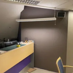 Biuro z recepcją w trakcie malowania ścian w odcieniach brązu i beżu, widoczne zabezpieczenia podłogi folią malarską i niedokończone łączenie kolorów na ścianie.