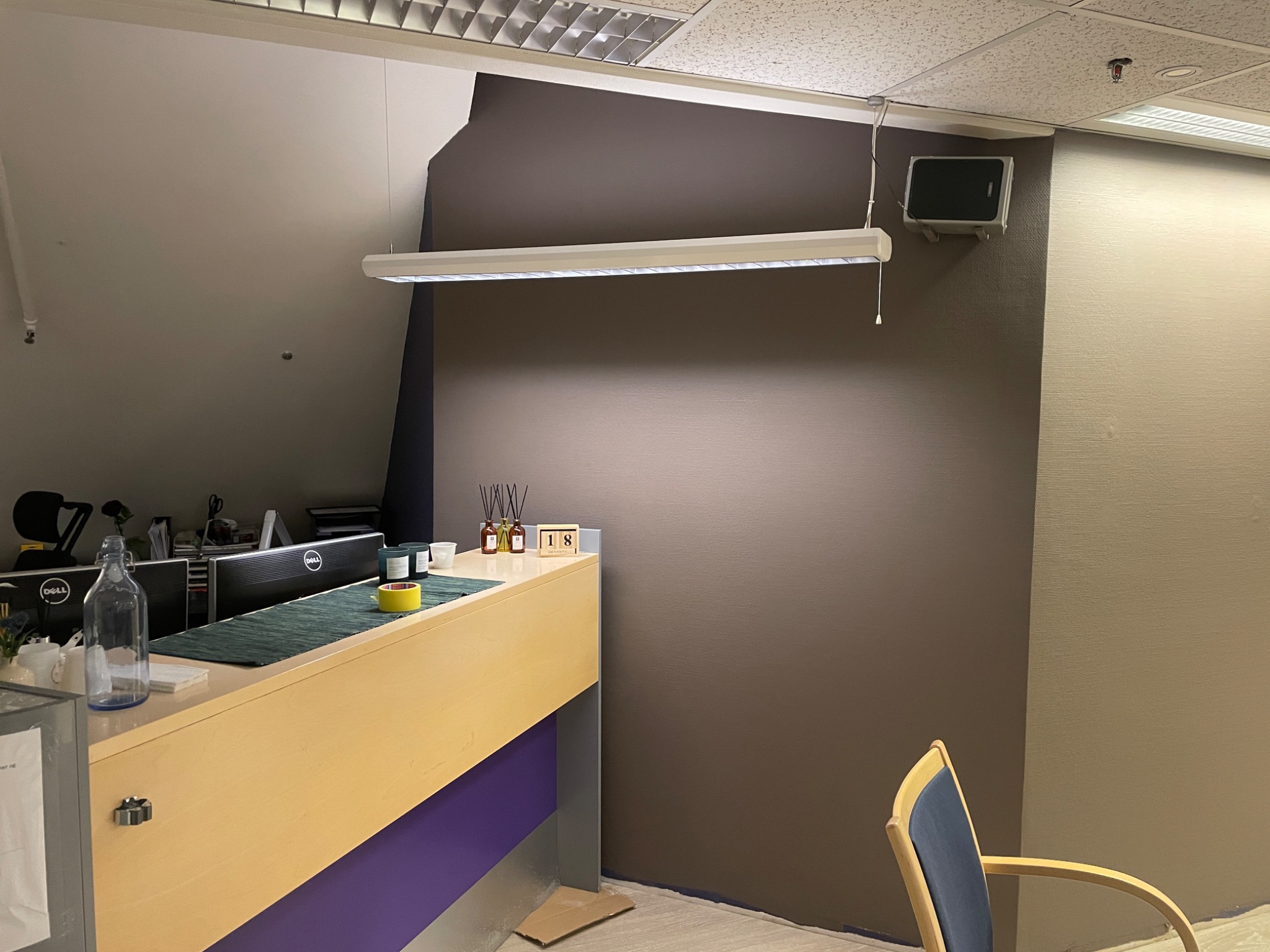 Biuro z recepcją w trakcie malowania ścian w odcieniach brązu i beżu, widoczne zabezpieczenia podłogi folią malarską i niedokończone łączenie kolorów na ścianie.