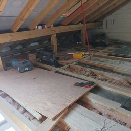 DreamBuilder - Poddasze w trakcie ocieplania z widoczną konstrukcją drewnianą, izolacją, narzędziami i płytą OSB na podłodze.