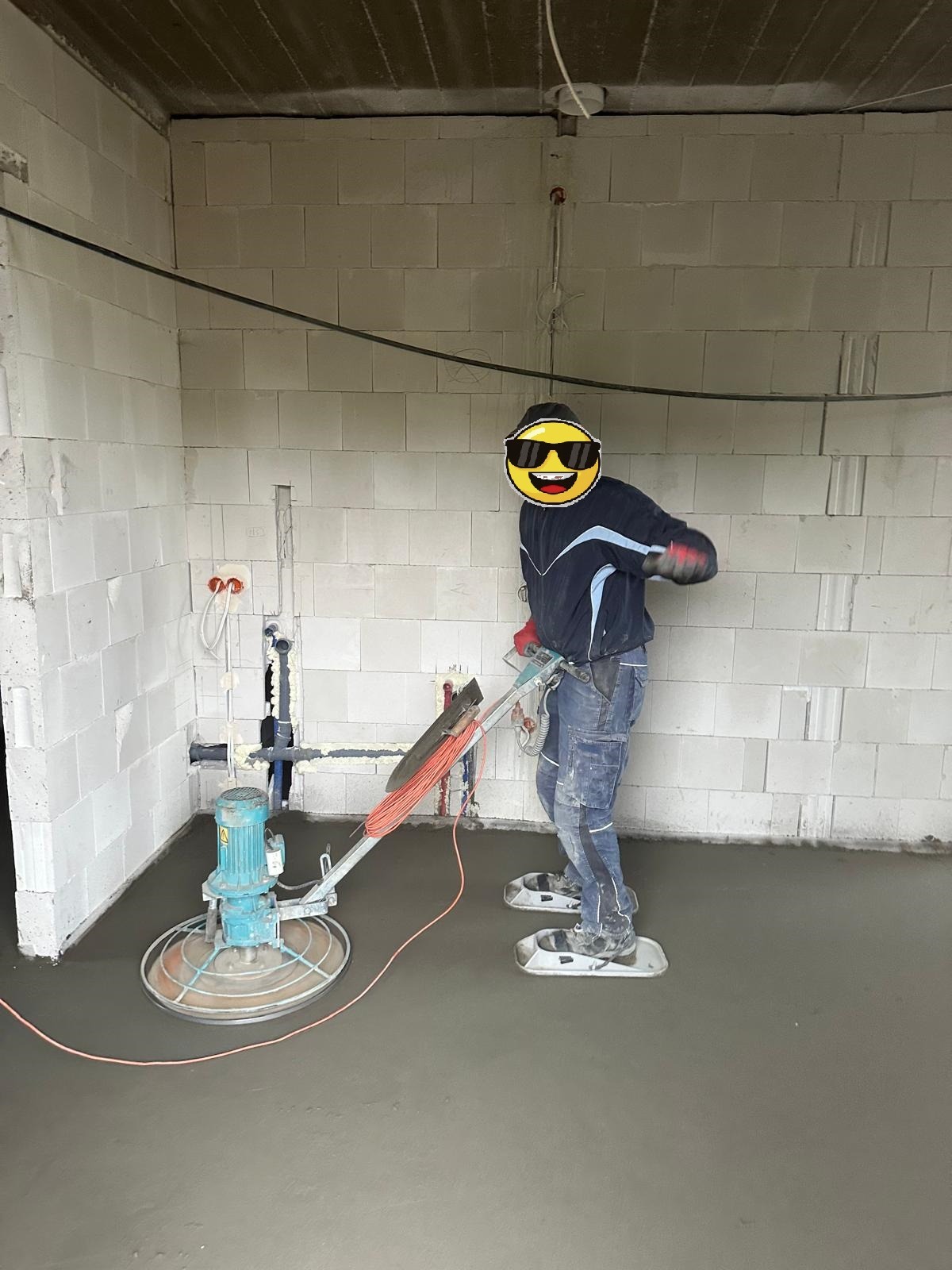 Pracownik w trakcie wygładzania posadzki jastrychowej za pomocą specjalistycznej maszyny w surowym wnętrzu budynku z białych bloczków.