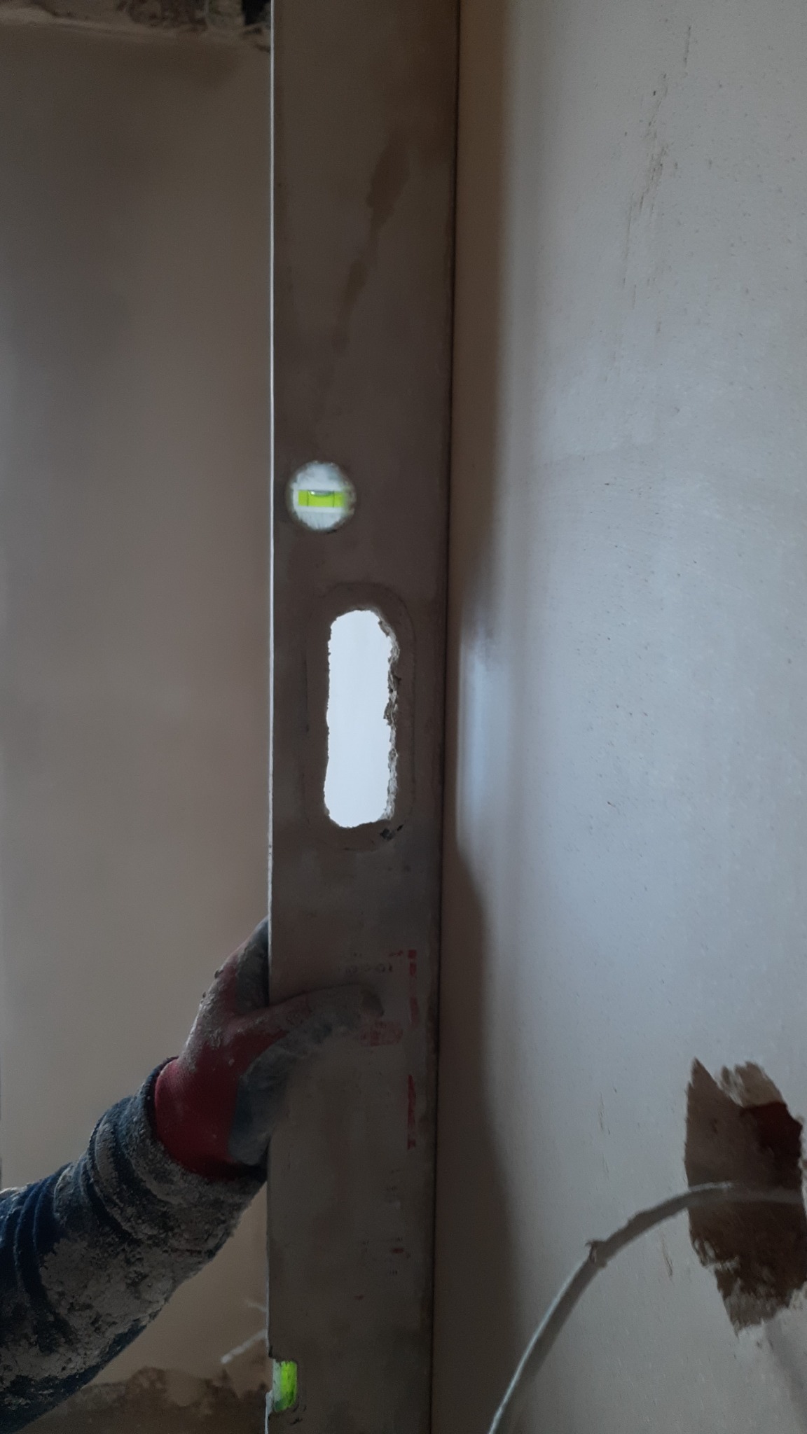 Poziomica przykładana do ściany podczas prac tynkarskich, widoczne ślady zaprawy i nierówności podłoża.