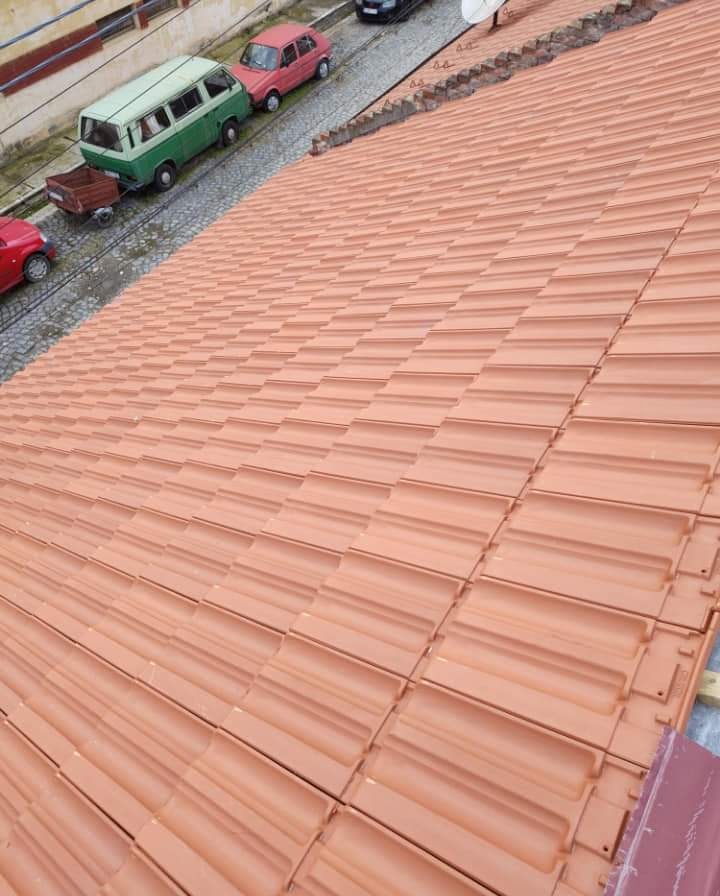 Nowy dach z czerwonej dachówki ceramicznej, widok z góry, z zaparkowanymi samochodami w tle.