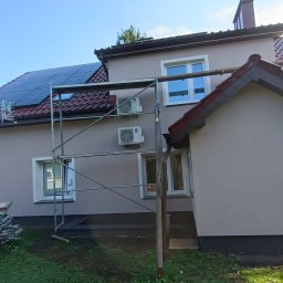 Zygmunt Czuba - Dom jednorodzinny z nową, jasnoszarą elewacją, widoczne rusztowania, panele słoneczne na dachu i klimatyzatory na ścianie budynku.