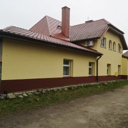 Zygmunt Czuba - Żółta elewacja domu z brązowym pasem u dołu i czerwoną dachówką, widoczny komin i klimatyzator na ścianie.