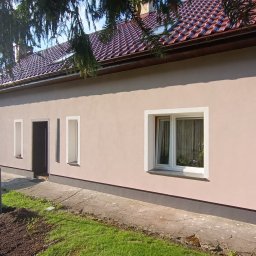 Zygmunt Czuba - Jasny, jednopiętrowy dom z nową, jasnoróżową elewacją. Widoczne białe obramowania okien i drzwi, brązowy dach z dachówki i częściowo zagospodarowany teren przed budynkiem. Na drugim planie drabina...