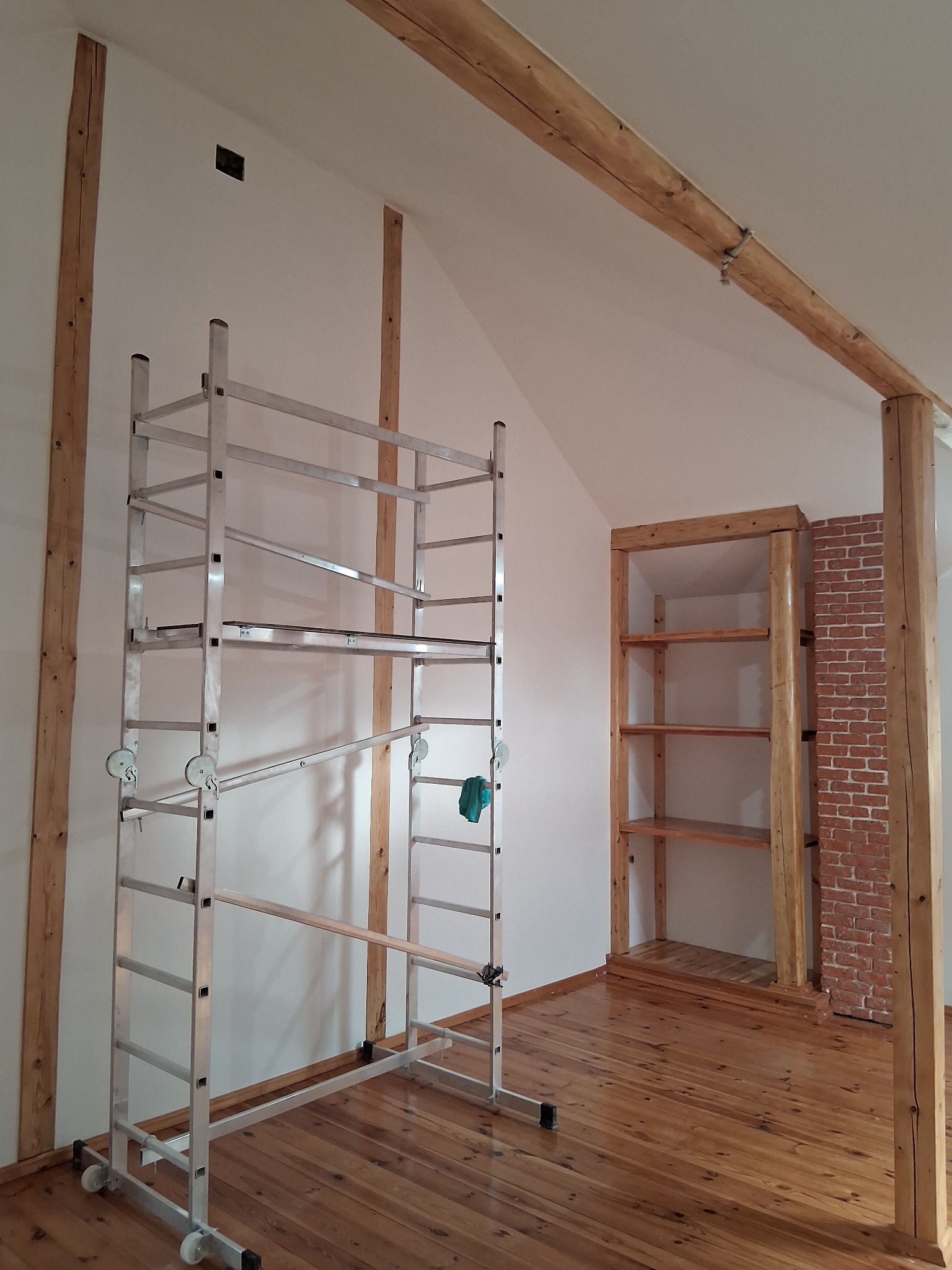 Wnętrze w trakcie prac wykończeniowych: drewniane elementy konstrukcyjne, regał z surowego drewna, rusztowanie aluminiowe, parkiet. Ściany przygotowane do malowania.