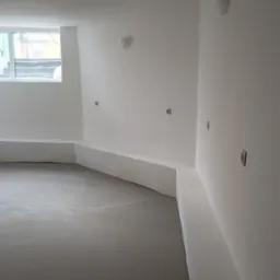 Wnętrze pokoju w Bełchatowie po wylaniu posadzki samopoziomującej, ściany przygotowane pod dalsze prace wykończeniowe, widoczne gniazdka elektryczne.