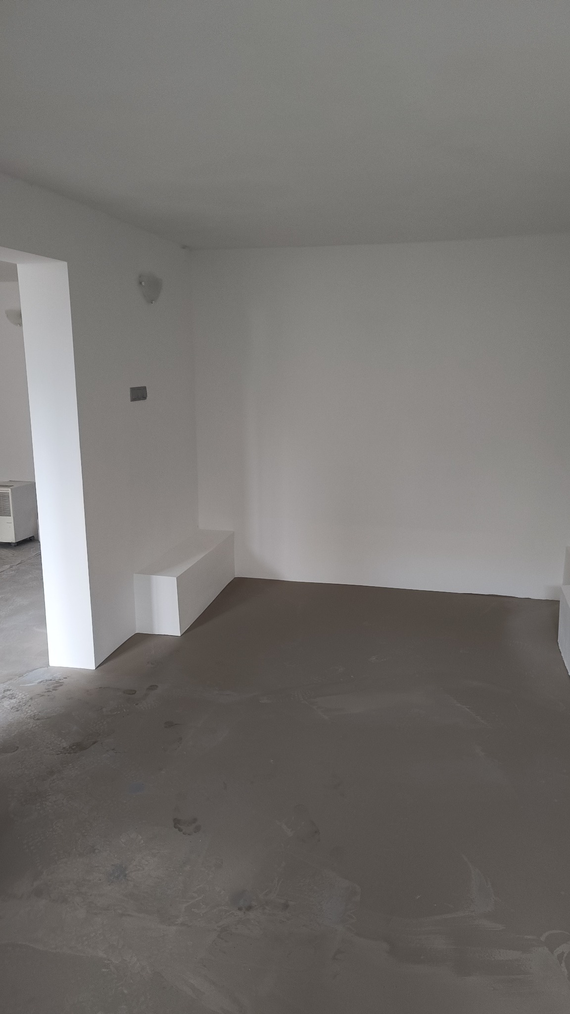 Przygotowane podłoże pod posadzkę w pustym, jasnym pomieszczeniu z białymi ścianami i wnęką.