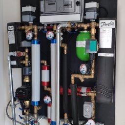 HydroMi Michał Jesionek - Kompletna instalacja hydrauliczna na ścianie z elementami marki Danfoss, widoczne rury miedziane, manometry, zawory, pompy obiegowe oraz sterownik elektroniczny.
