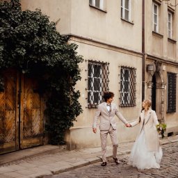 Paulina Rasińska Fotografia - Para młoda trzymająca się za ręce na brukowanej uliczce Starego Miasta, obok kamienicy z drewnianymi drzwiami obrośniętymi bluszczem i ozdobnymi oknami.