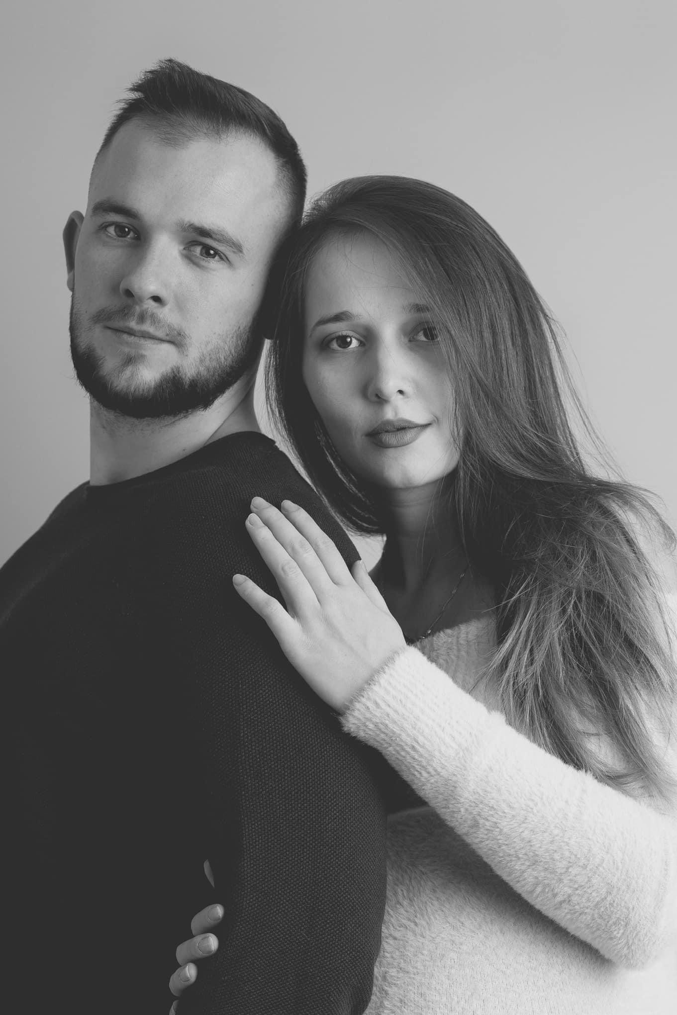 Czarno-białe portretowe zdjęcie pary: mężczyzna z brodą i kobieta z długimi włosami, ona opiera dłoń na jego ramieniu, oboje patrzą w obiektyw.