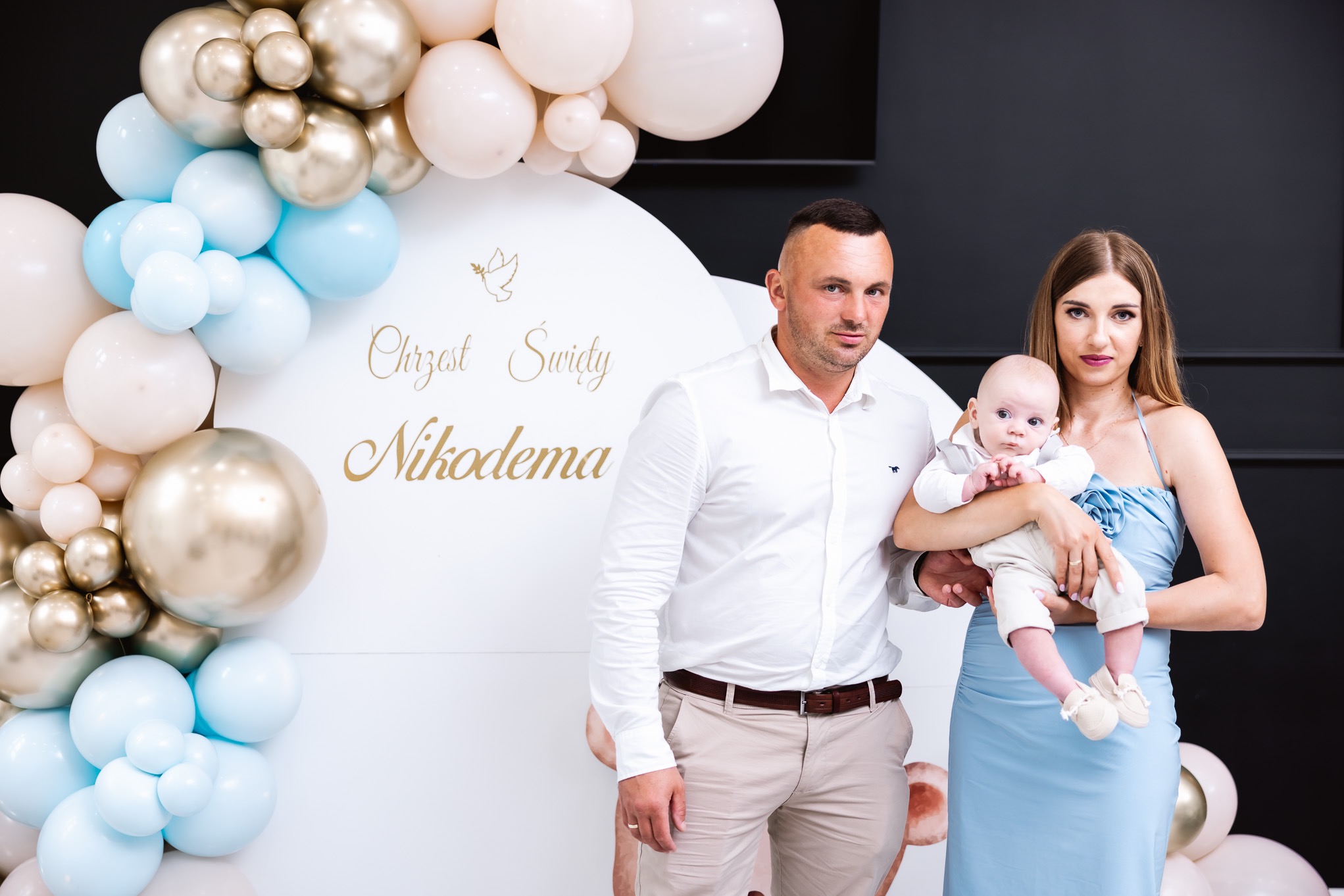 Rodzinne zdjęcie z uroczystości Chrztu Świętego Nikodema na tle dekoracji z białych, złotych i błękitnych balonów.