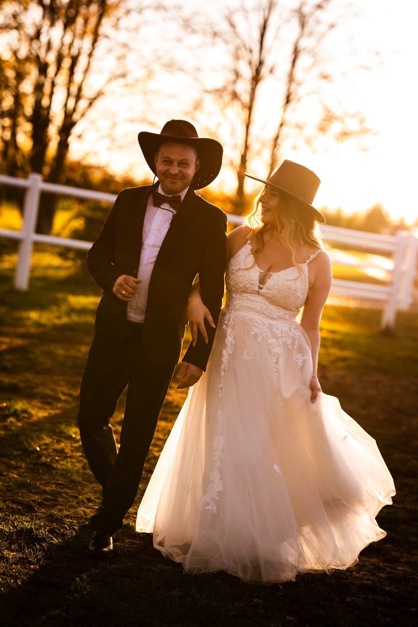 Para w strojach ślubnych w stylu kowbojskim spaceruje po łące o zachodzie słońca. Ona w białej sukni, on w czarnym garniturze i muszce. Oboje w kapeluszach.