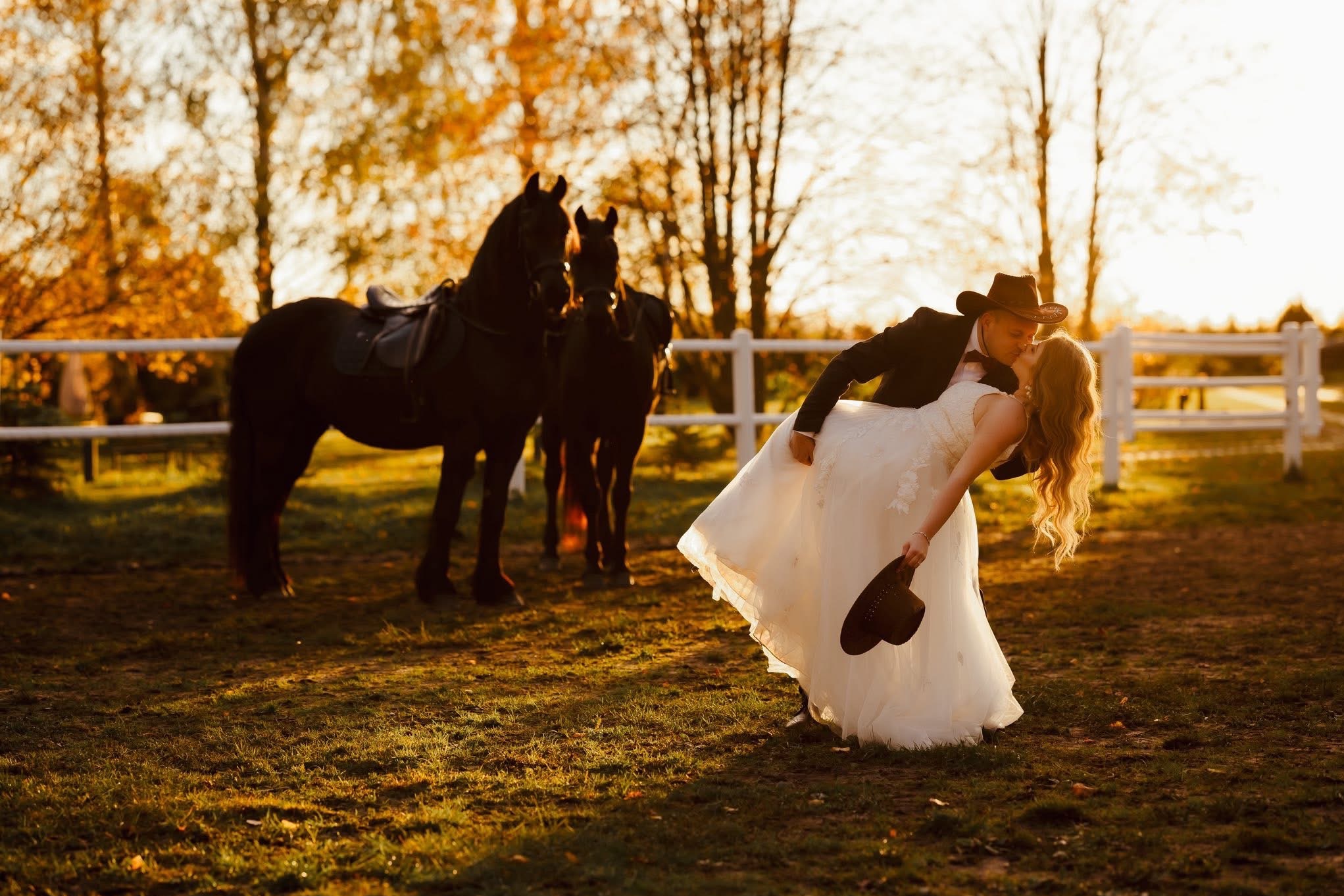 Romantyczny pocałunek pary młodej w stylu kowbojskim na tle koni i zachodzącego słońca w Busko-Zdroju. Sesja plenerowa z unikalnym motywem.